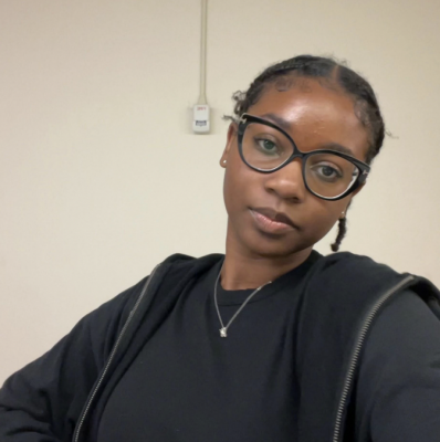 A photograph of Mikayla, a Black girl with glasses looking directly at camera. 